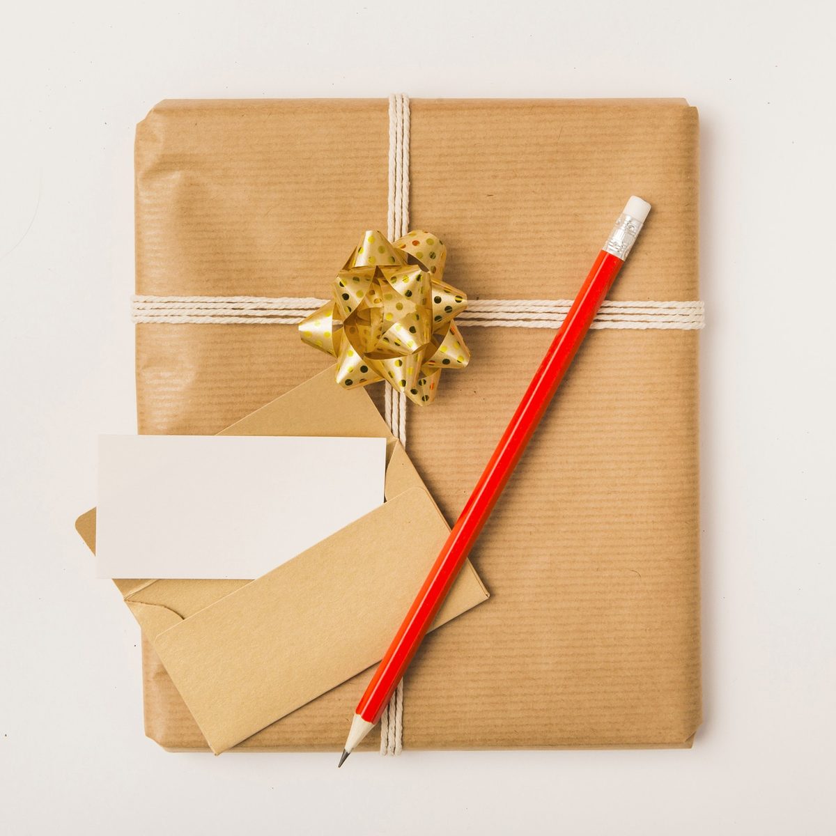 Cream birthday card, a gold pen and a small wrapped gift with a silk ribbon on a white linen tablecloth