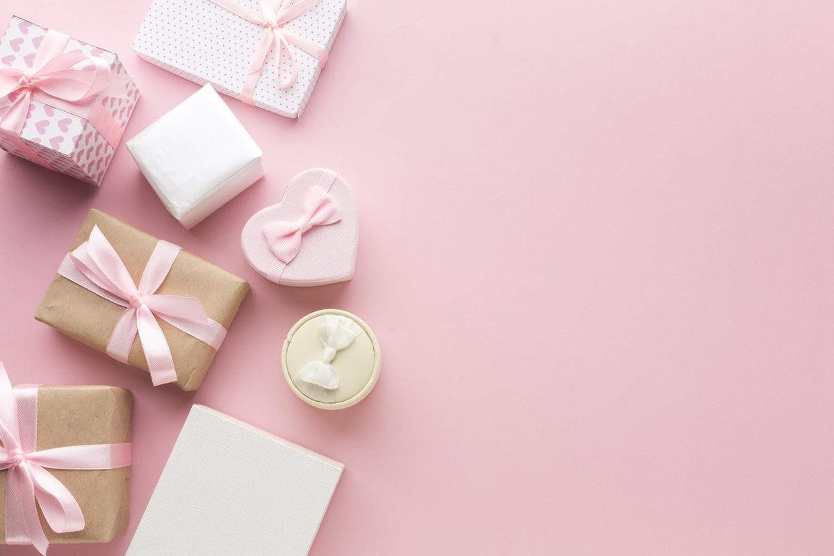 Pastel balloons and a blush gift box with a satin bow on a light wooden table