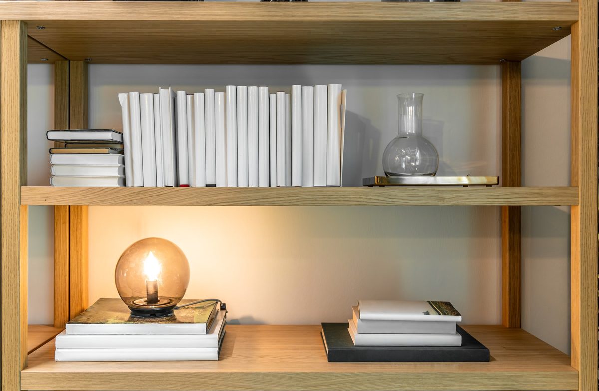 Light wood bookshelf with white books and a warm glowing lamp in a cozy corner