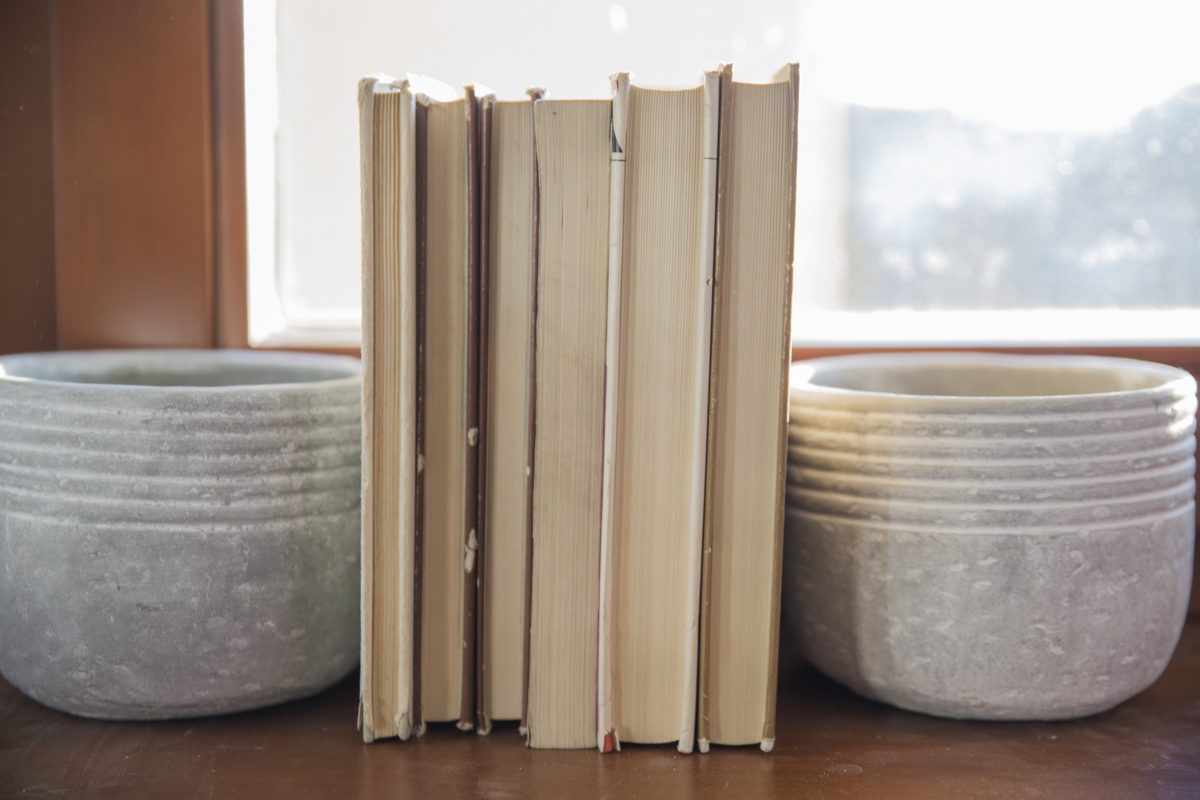 Row of upright cream books between two textured ceramic pots on a wooden shelf