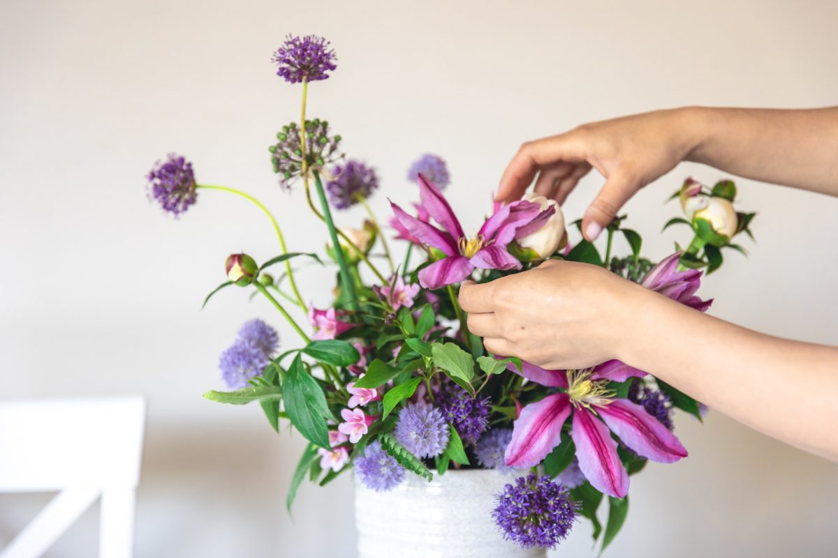 Woman's hands arranging fresh flowers in a white vase, close-up
