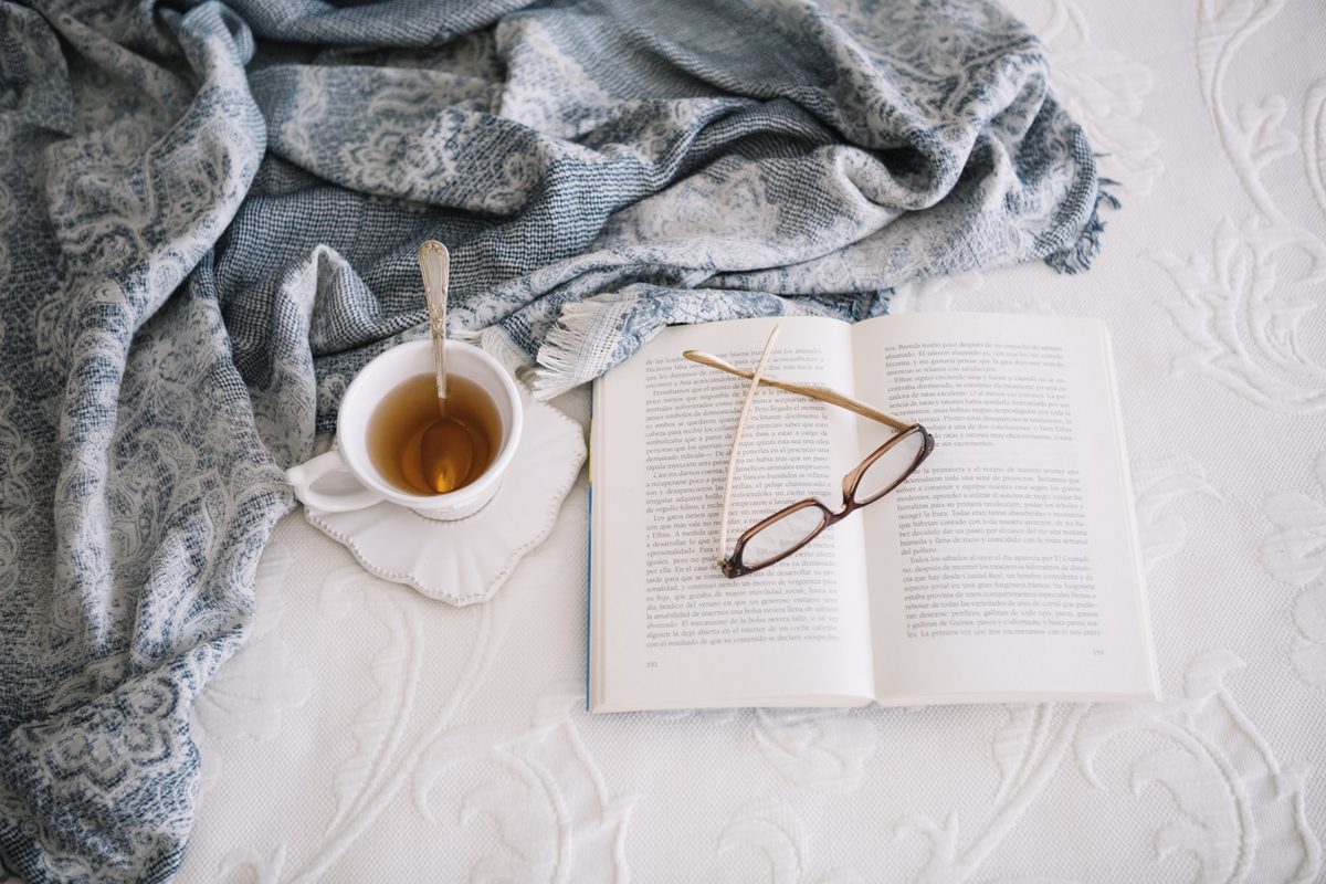 Lavender eye pillow, a cup of herbal tea and an open journal on a white bed in soft evening light