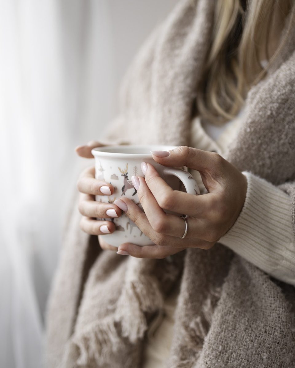 Woman's hands resting on her lap over a cream knit sweater while sitting on a white bed