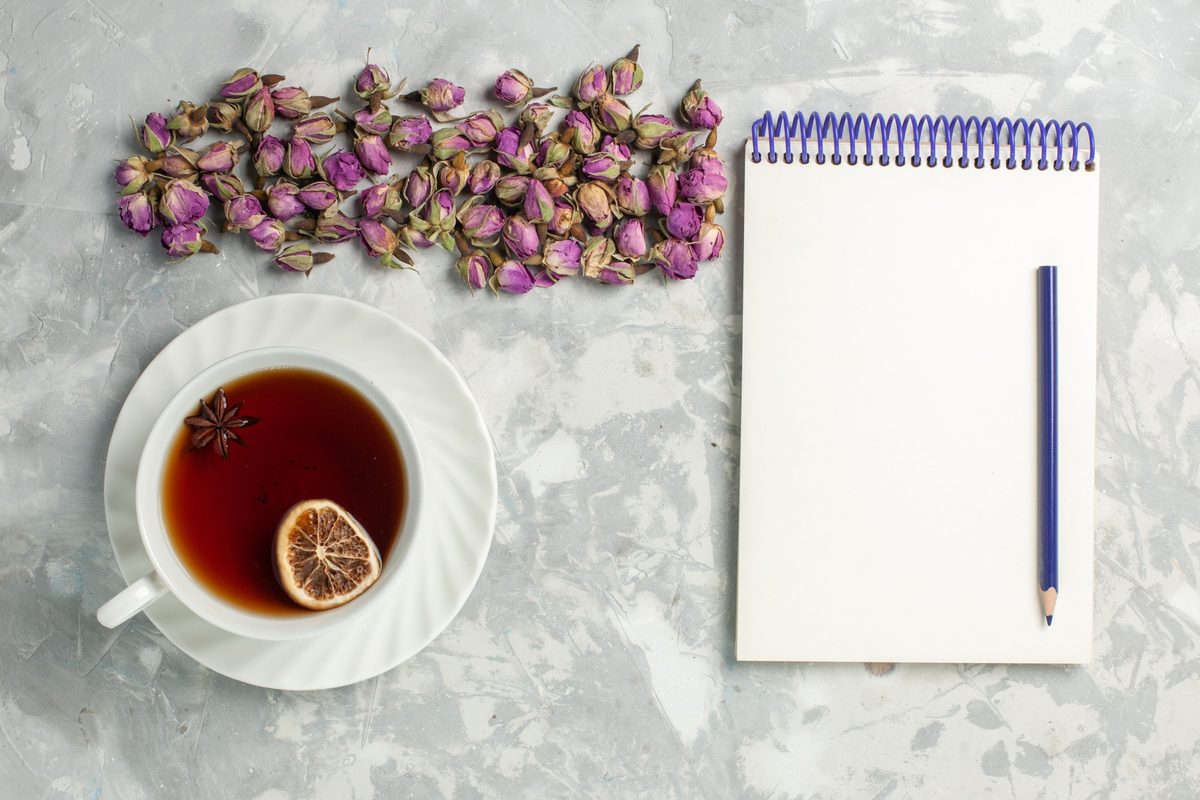 Blank spiral notepad, a pencil and a cup of tea with dried rosebuds on a light gray desk