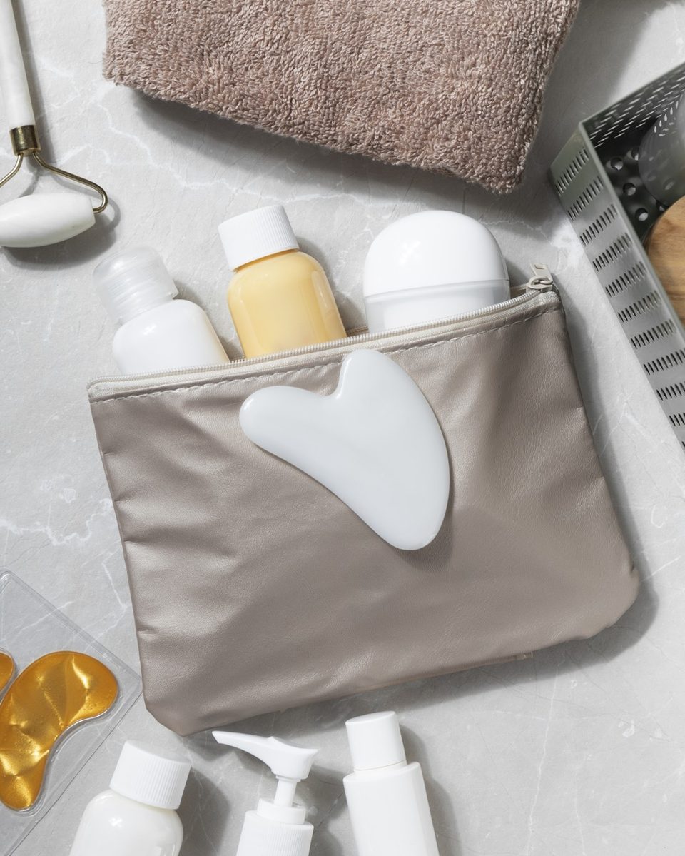 Clear toiletry bag with small travel bottles, a lip balm and a hand cream on a white bathroom counter