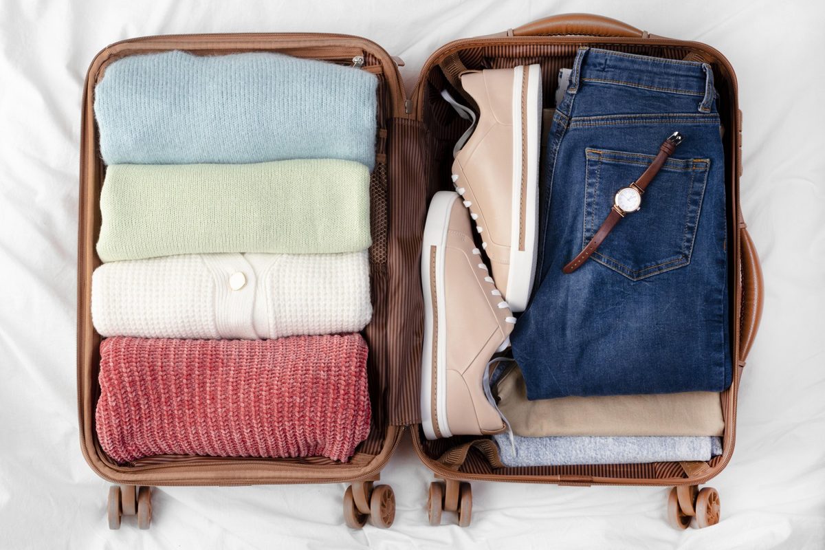 Open carry-on suitcase neatly packed with beige packing cubes, folded women's clothes and a pair of white sneakers
