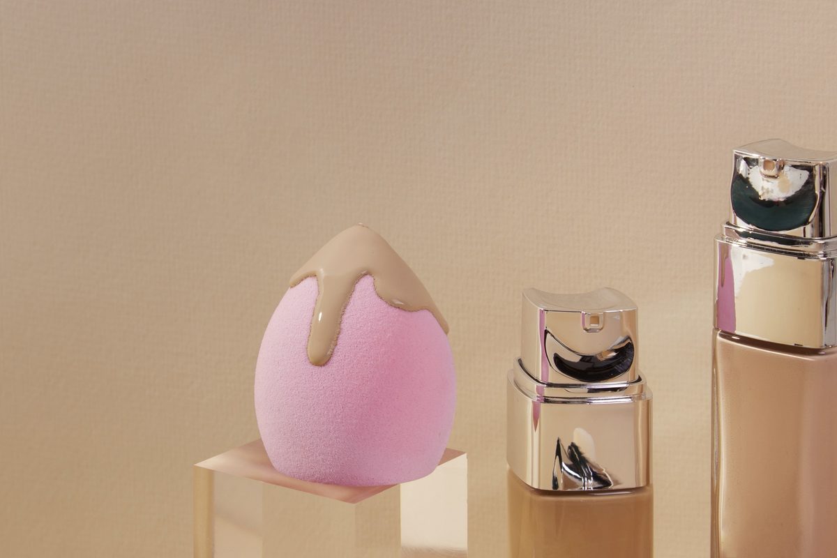 Pink beauty sponge beside two liquid foundation bottles on a beige background