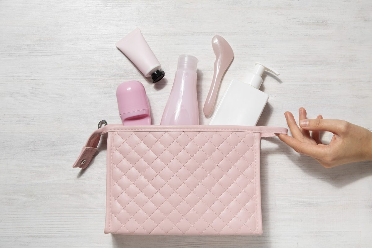 Pink quilted makeup bag with skincare and cosmetics spilling out and a woman's hand