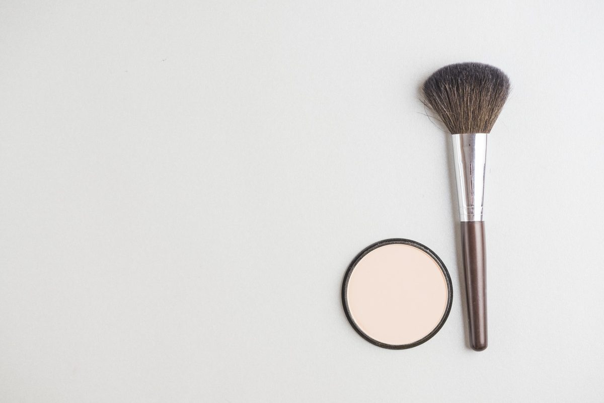 Pressed powder compact and a fluffy powder brush on a white surface