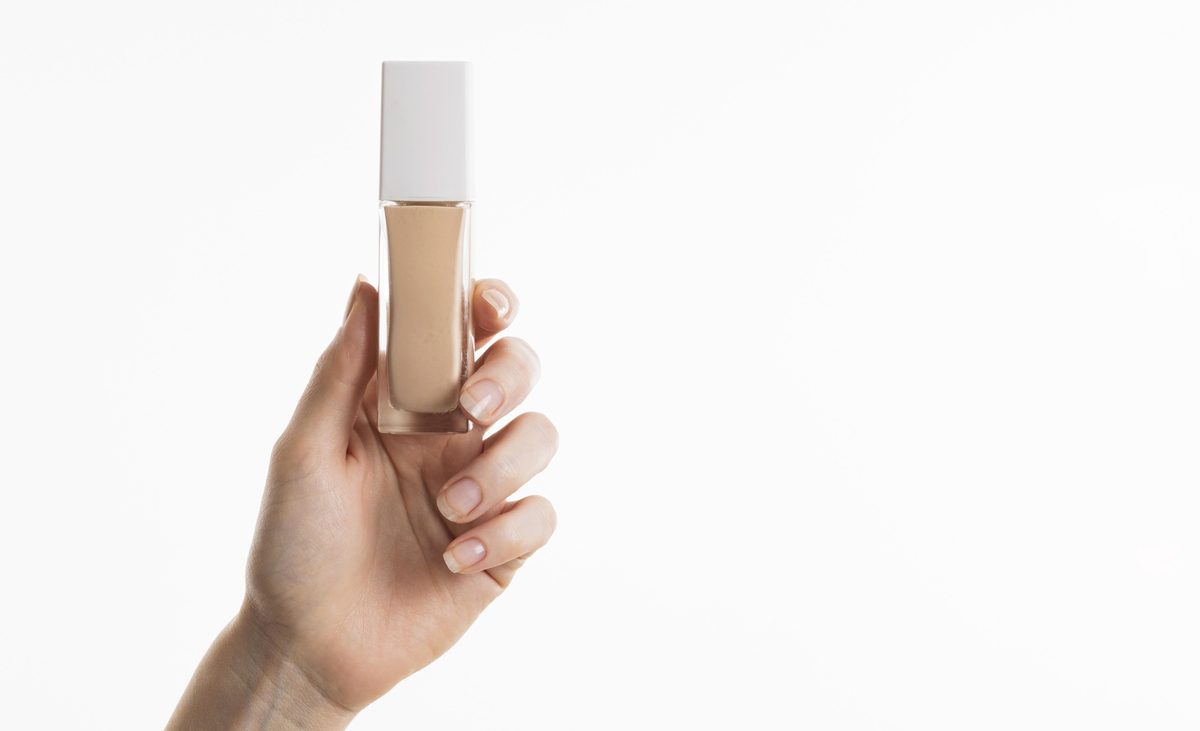 Woman's hand holding a liquid concealer bottle against a white background