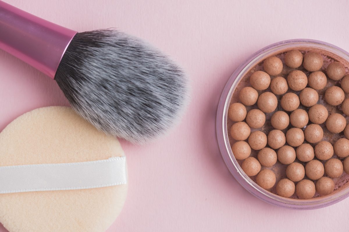 Bronzing pearls, a pink-handled makeup brush and a powder puff on a pink background