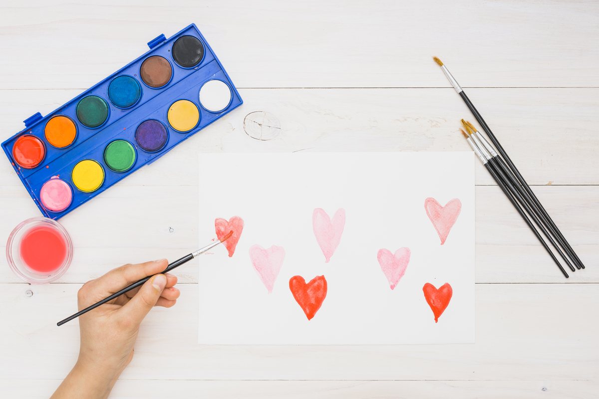 Hand painting small pink and red watercolor hearts on white paper