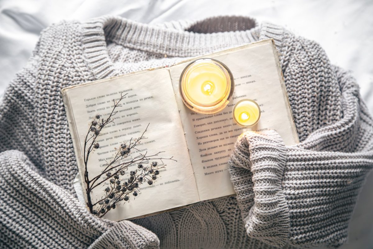 Open notebook, a pen and a lit candle in a glass jar on a cream bedside table in soft evening light