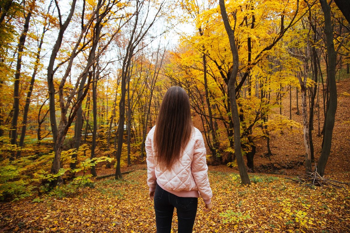 Woman seen from behind walking on a quiet tree-lined path in soft autumn light