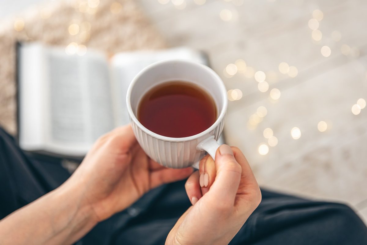 Woman's hands holding a warm cup of tea over a soft cream blanket in gentle morning light