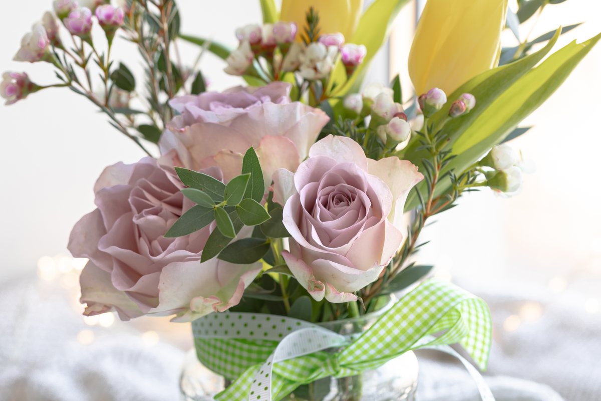 Pastel roses and yellow tulips in a glass jar tied with a green ribbon