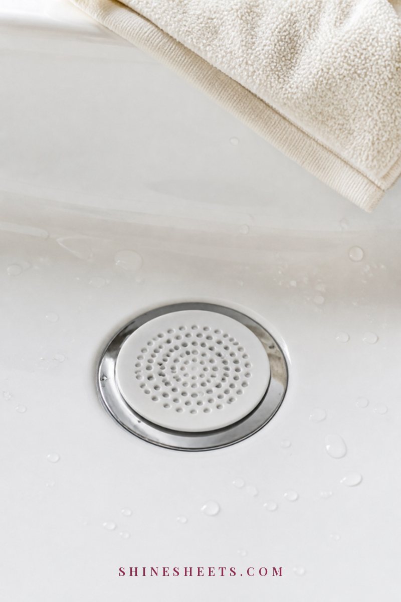 A shiny chrome bathtub drain with a neat round hair catcher in a spotless white tub, soft light