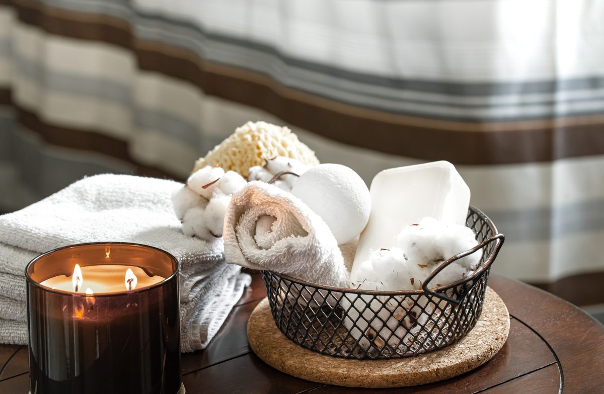 Lit candle and rolled white towels in a wire basket on a bathroom table