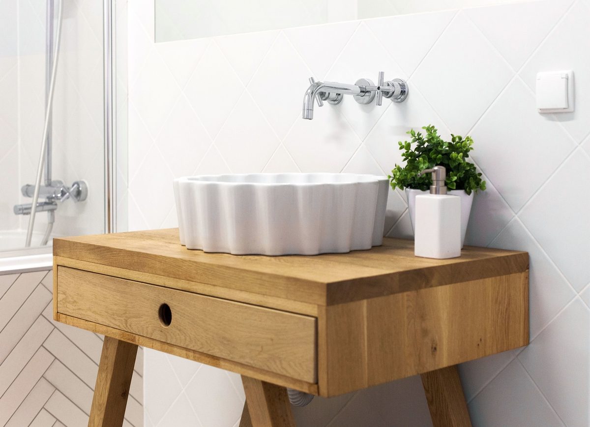 White vessel sink on a wooden vanity with a small potted plant in a bright bathroom