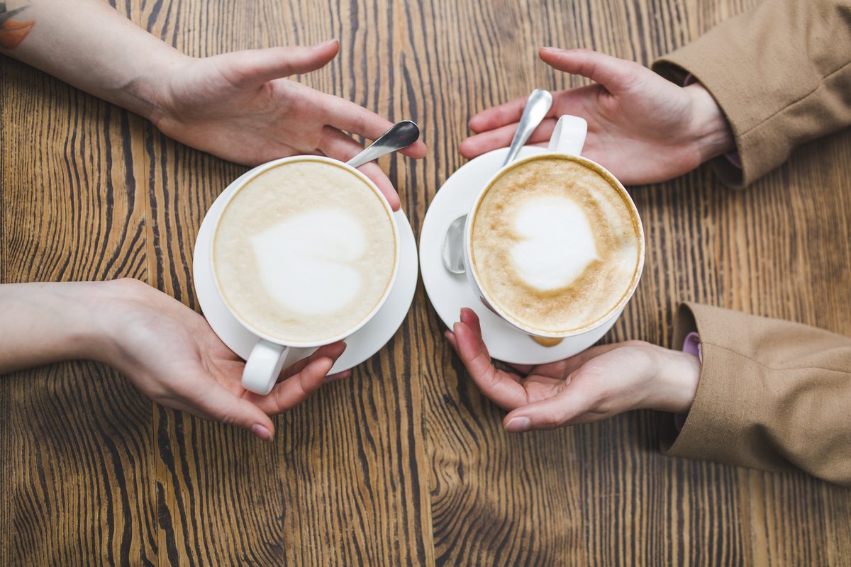 Two friends sharing coffee with heart latte art at a rustic cafe table