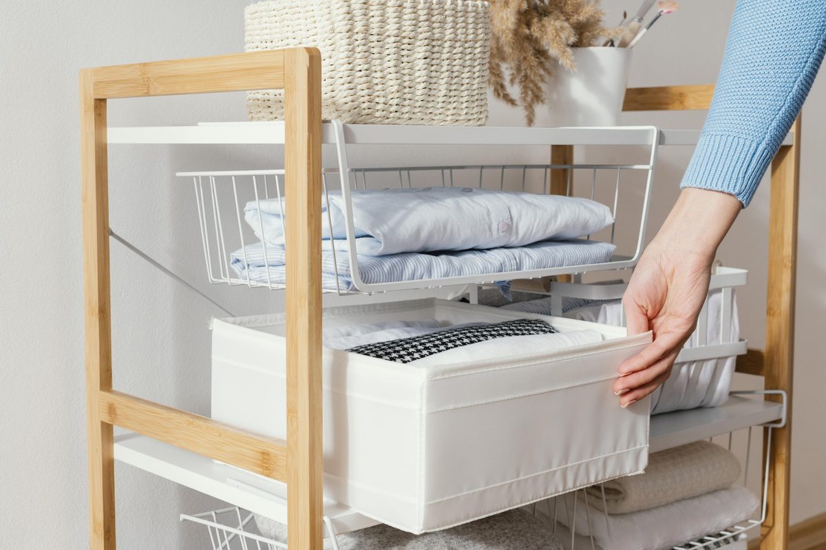 Bamboo shelving unit with wire baskets and folded clothes, a woman's hand reaching in