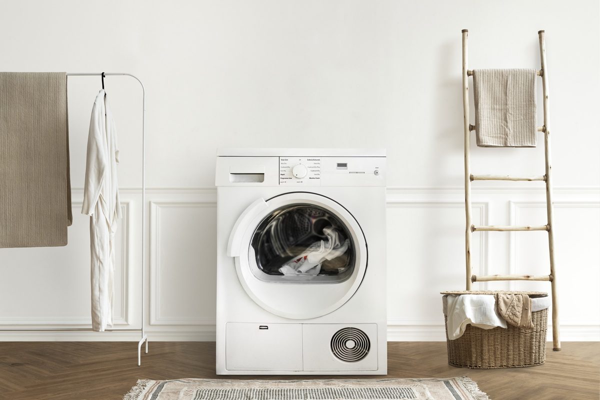 Minimal white laundry room with a washing machine, a ladder towel rail and a woven basket