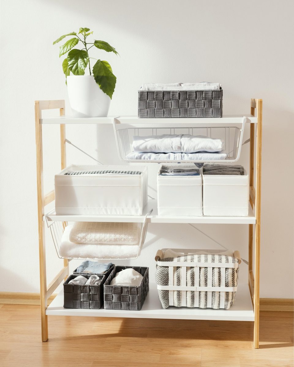 Bamboo shelving unit with folded linens, baskets and a plant in a bright room