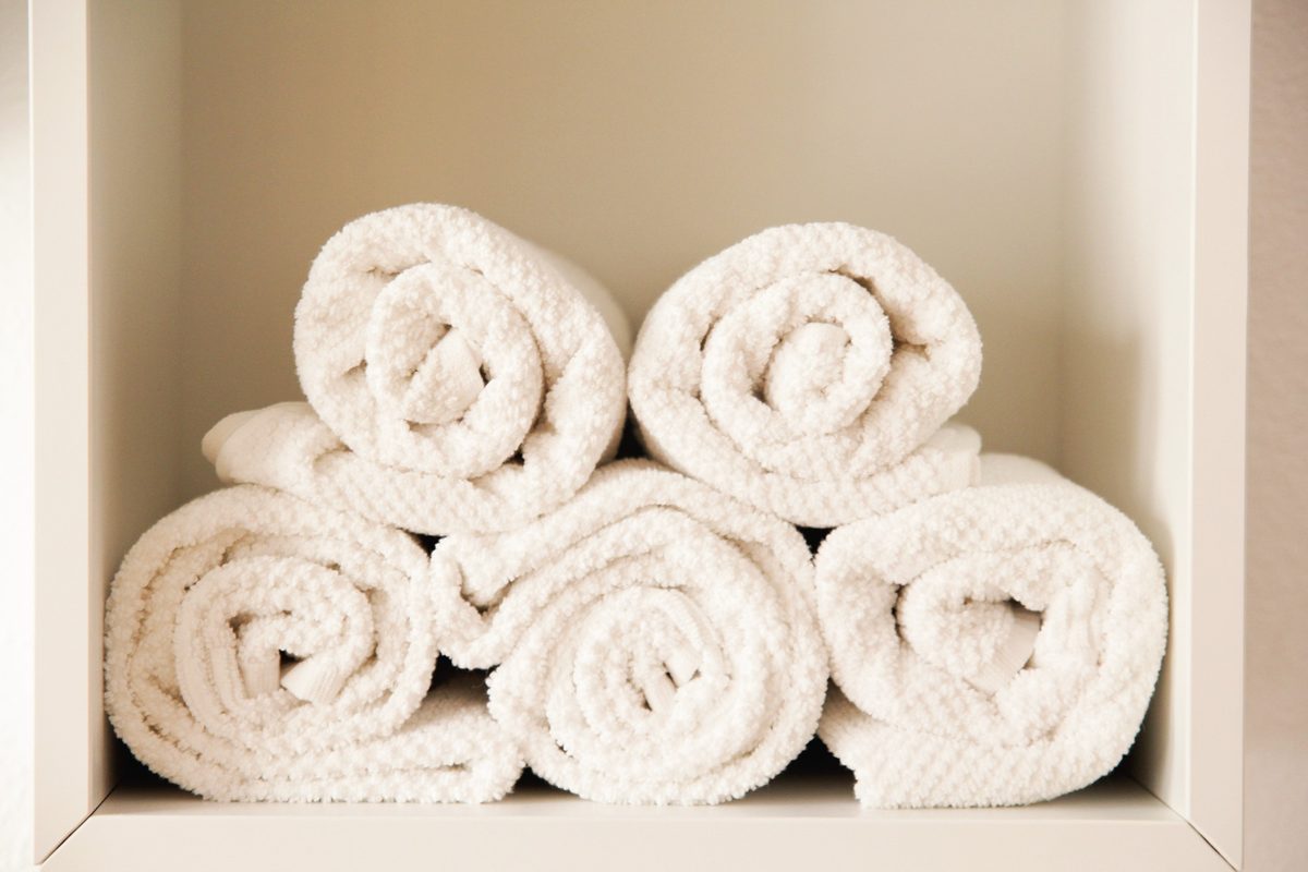 Rolled cream bath towels on a white shelf
