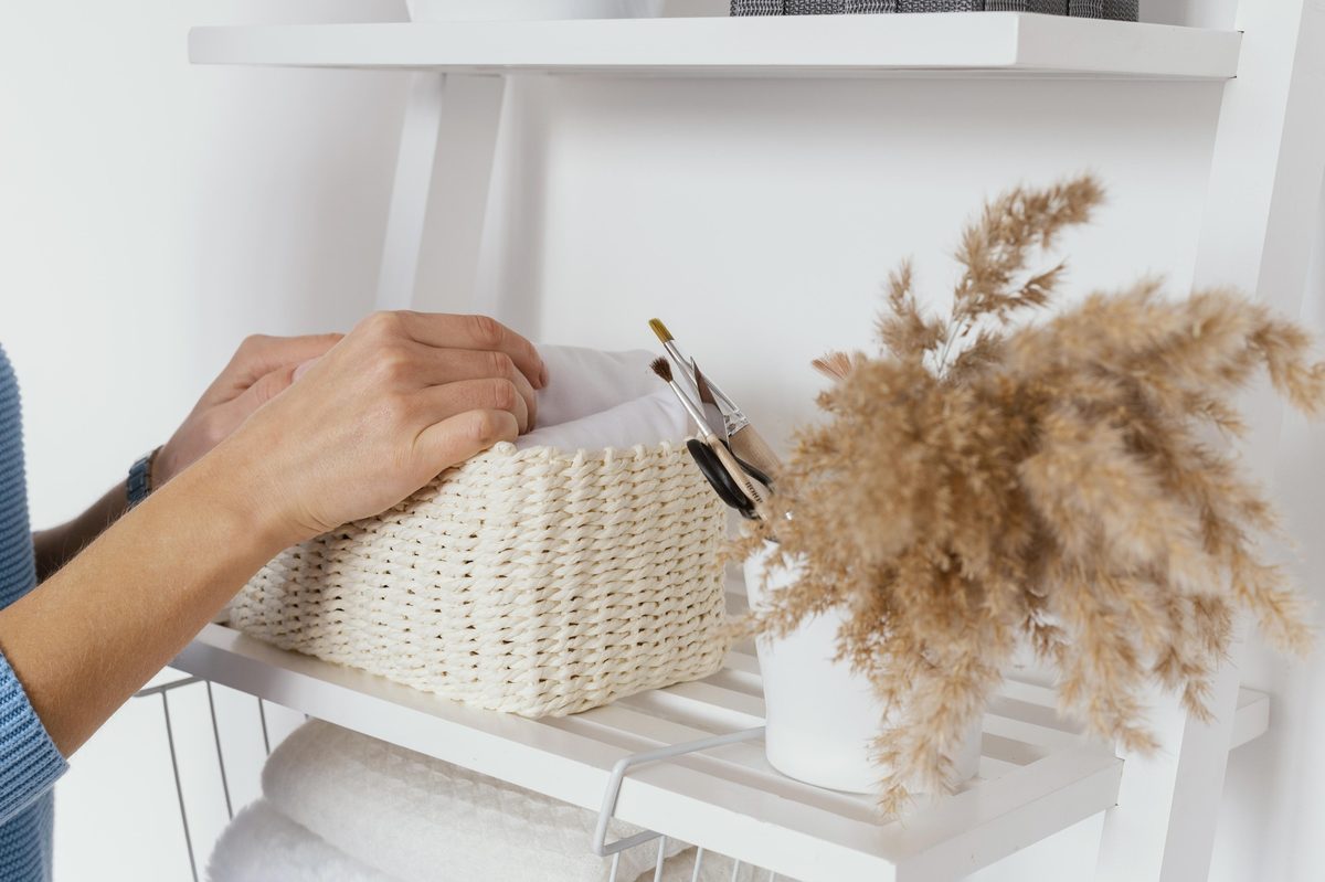 Woman's hand placing a woven basket on a white shelf next to dried pampas grass