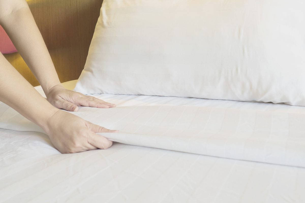 Woman's hands smoothing a crisp white sheet on a bed