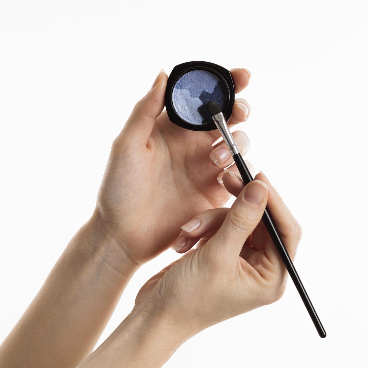 Cropped view of a woman's hand holding a fluffy blending brush over a rosy eyeshadow palette on a white table