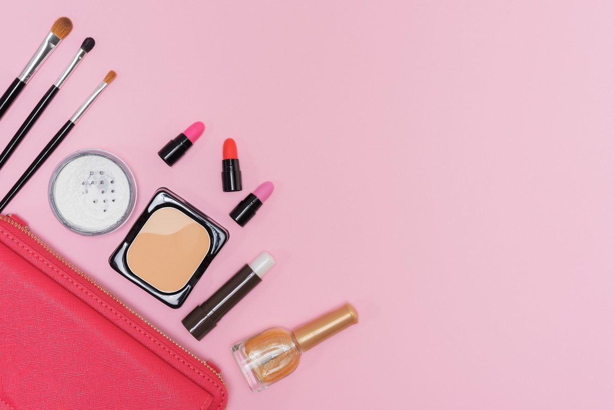 Open eyeshadow palette in mauve, plum and copper shades with two makeup brushes on a cream vanity tray
