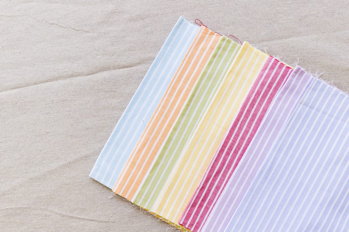 Flat lay of fabric swatches in blush, cream and sage with stripes, gingham and small florals on a linen surface