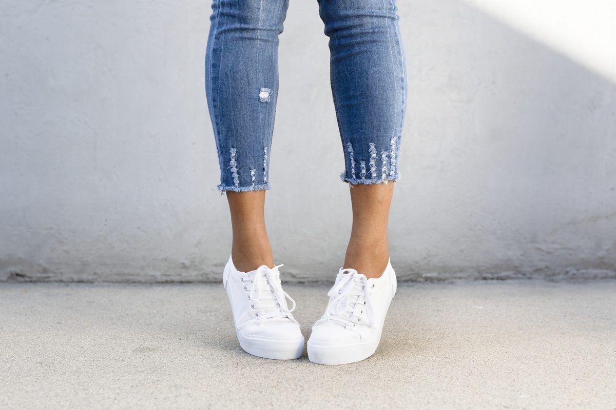White women's sneakers, folded beige leggings, a cream water bottle and a knit headband laid out on a wooden floor