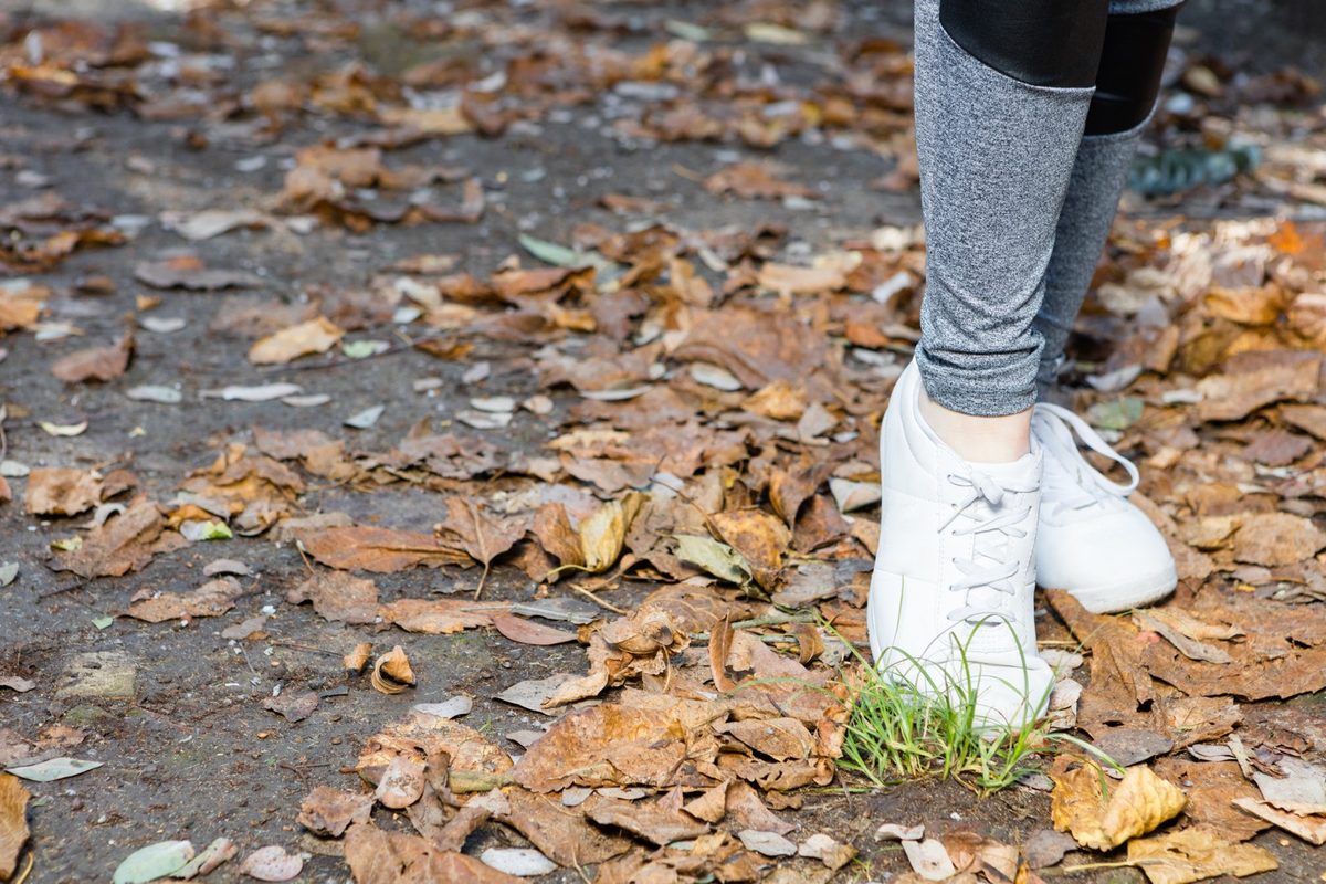 Women's feet in white sneakers on a misty park path covered with autumn leaves