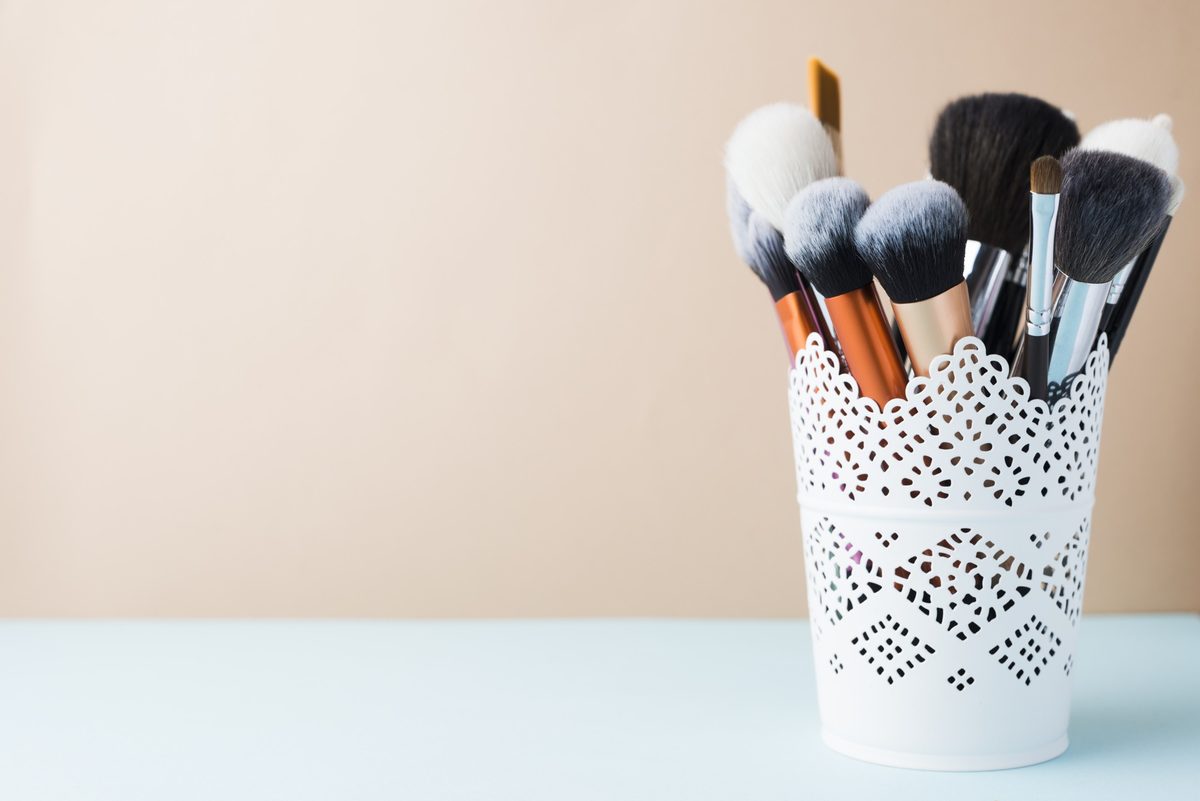 Makeup brushes in a white lace cup on a pastel table
