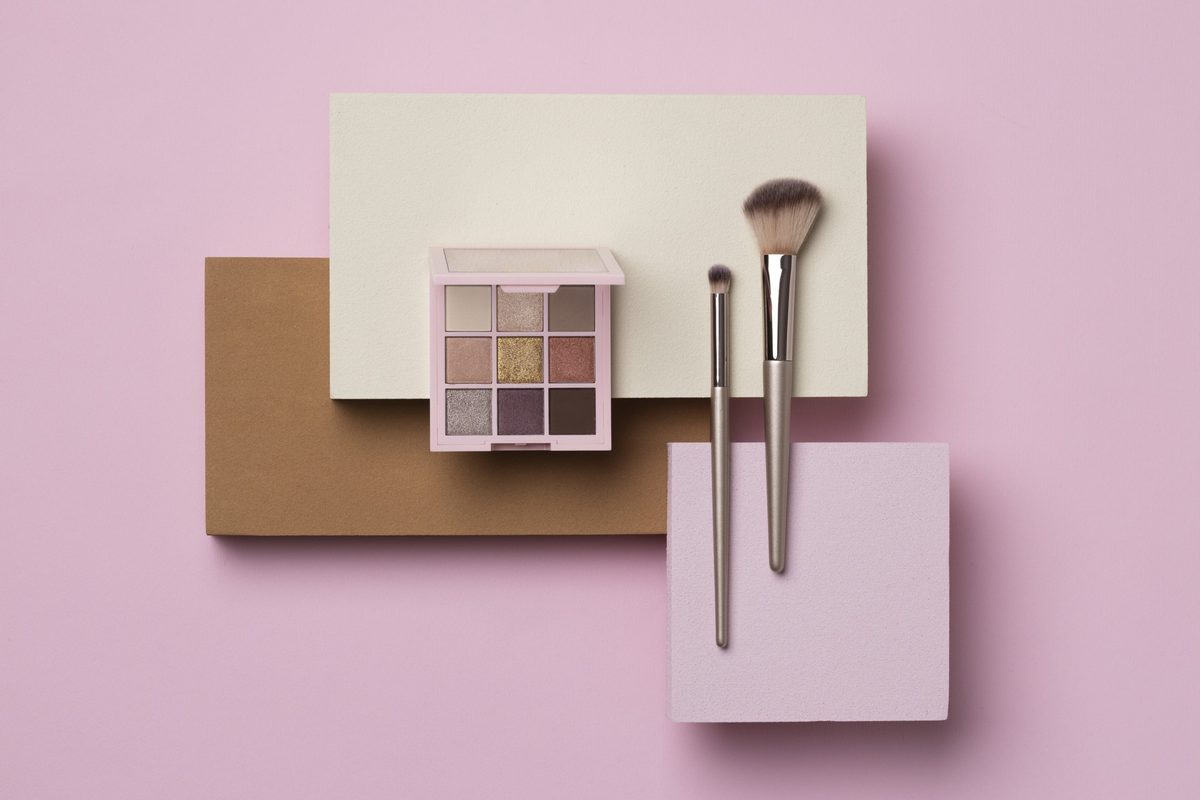 Neutral eyeshadow palette and two makeup brushes on blush paper