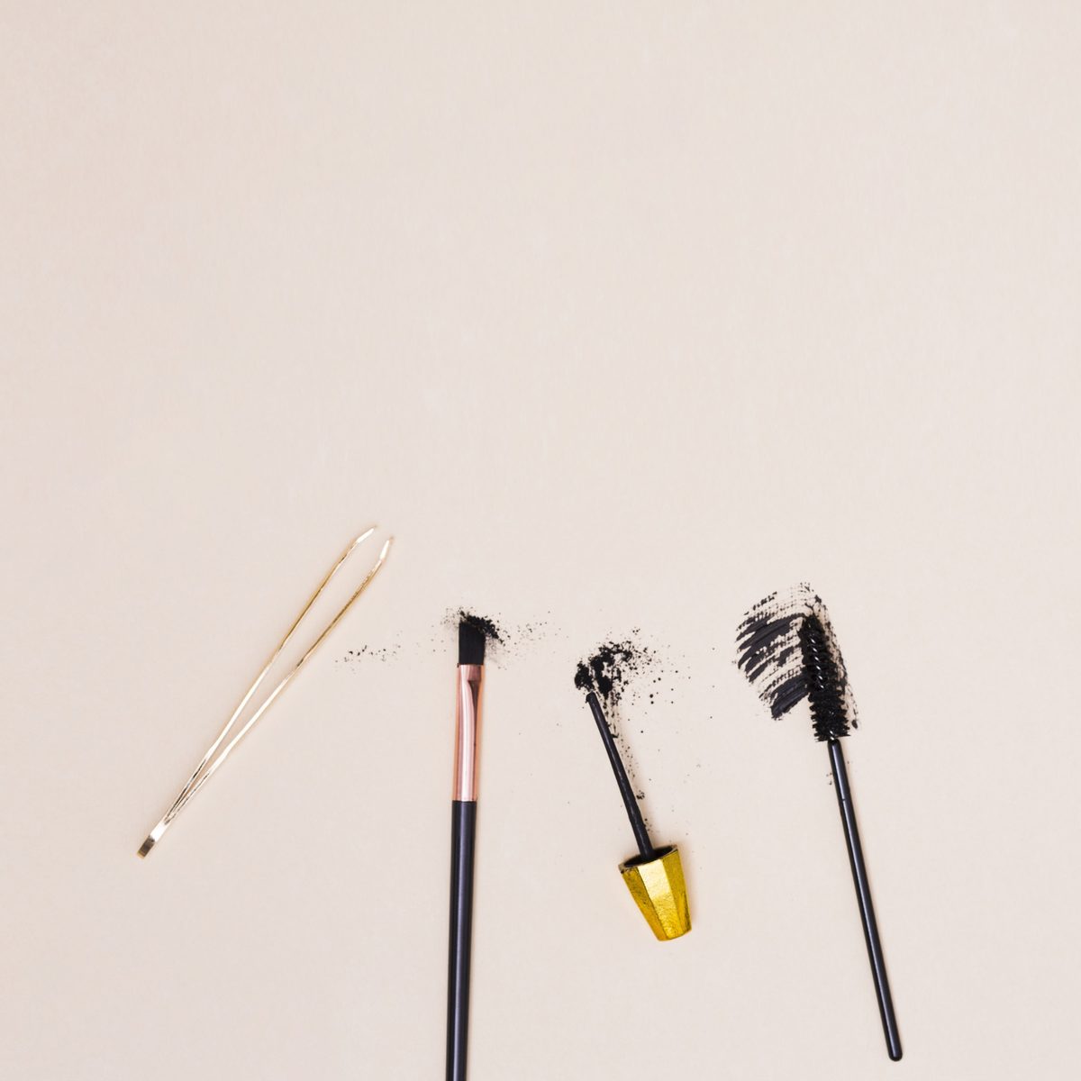 Tweezers, a brow brush, a mascara and a spoolie on a beige background