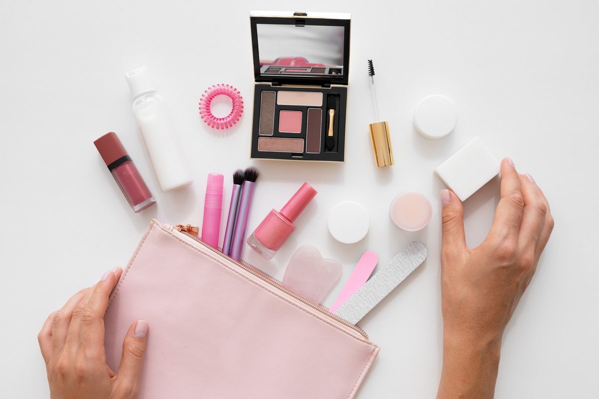 Woman's hands taking cosmetics out of a pink makeup bag on a white table