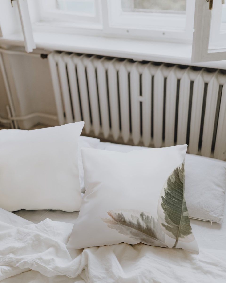 Neutral bedroom with layered cream and oatmeal bedding, a linen headboard and a wooden nightstand with a small lamp