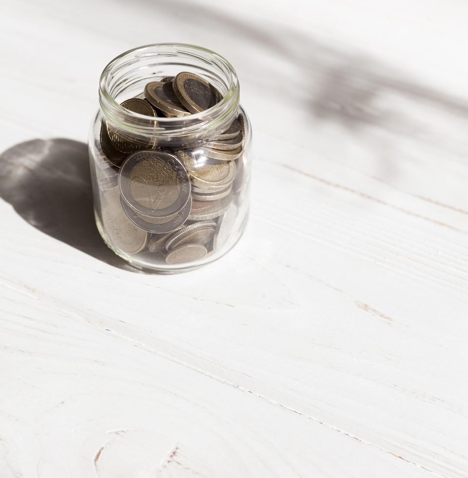 Glass jar of coins on a white wooden table in soft light