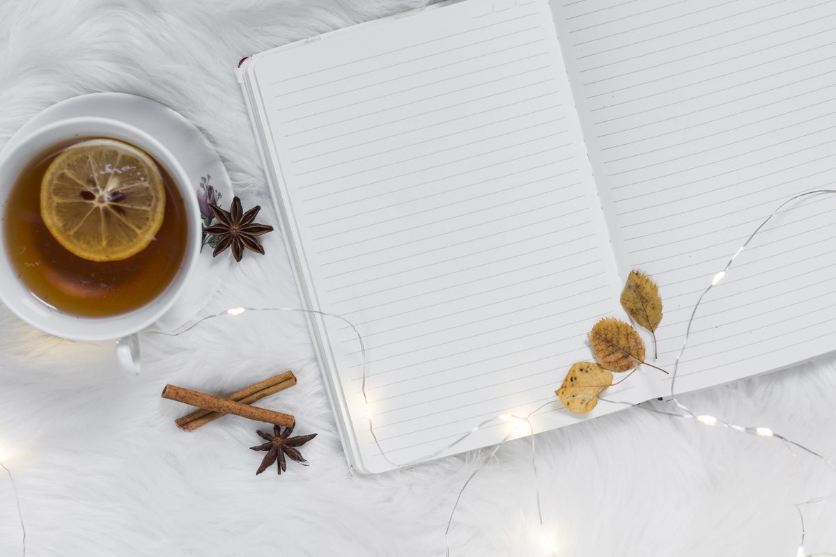 Open notebook and a cup of lemon tea on a fluffy white blanket with fairy lights
