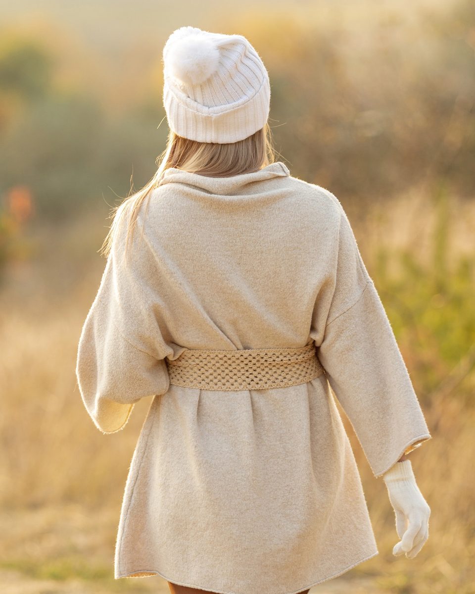 Woman in a cream coat and beanie seen from behind walking through an autumn field