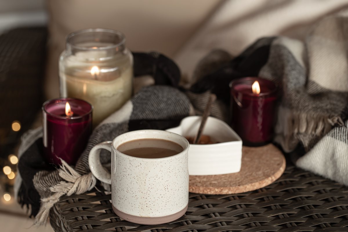 Mug of coffee with glowing candles and a soft blanket on a cozy evening