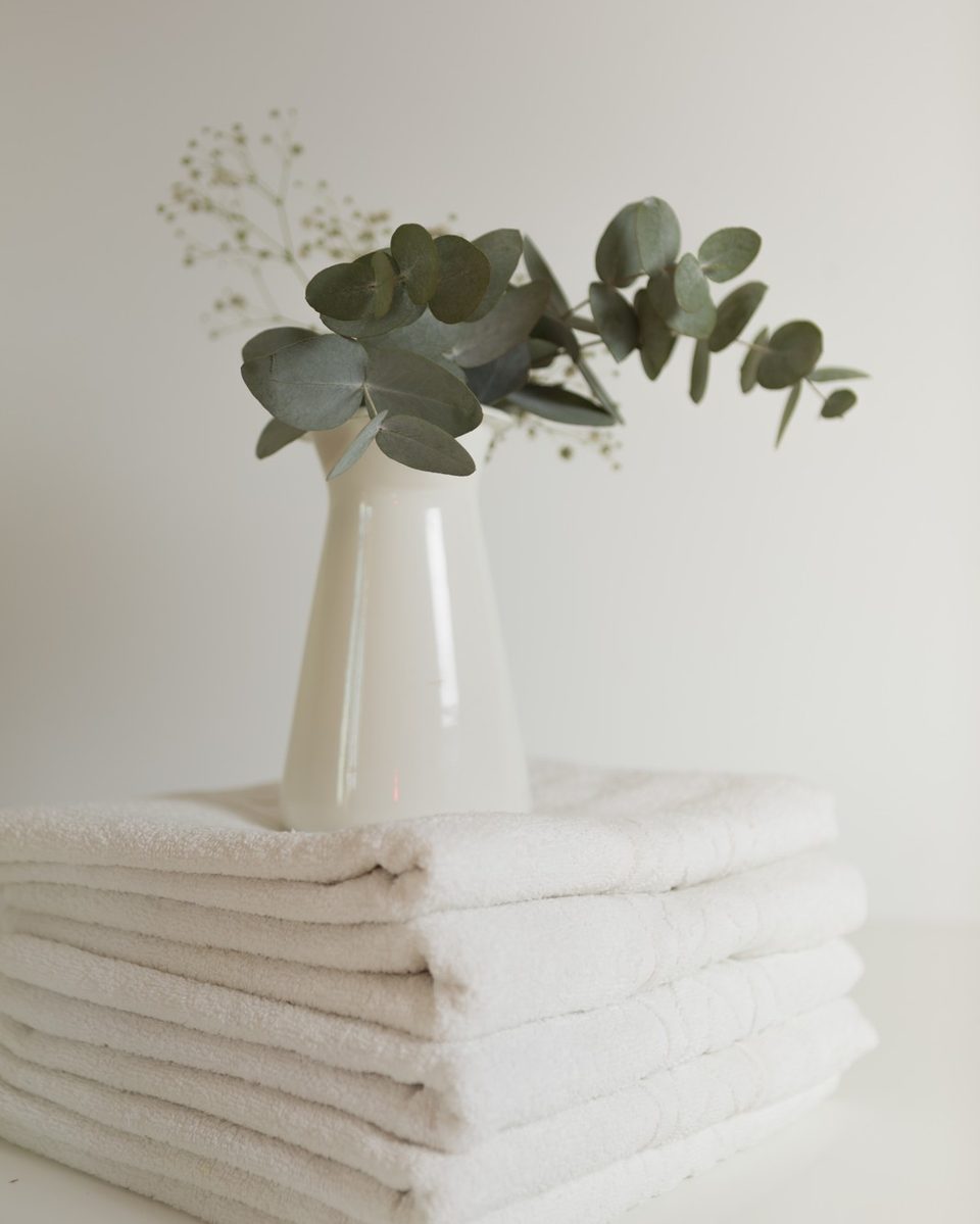 White over-the-toilet shelf styled with rolled cream towels, a woven basket, a small plant and a glass candle