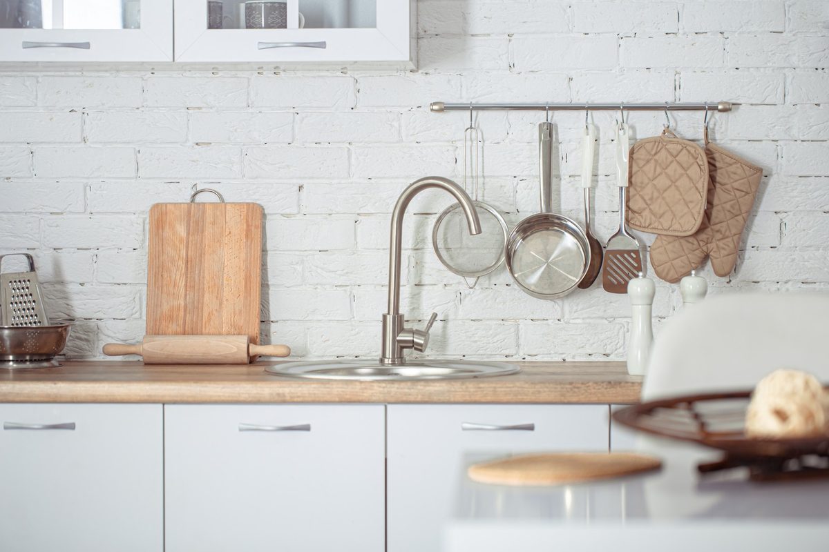 Bright small kitchen with white cabinets, gold knobs, glass canisters and a wooden cutting board leaning on the counter