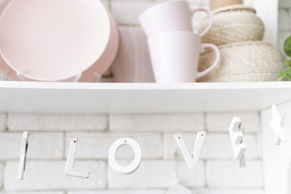 Open wooden kitchen shelf styled with stacked cream plates, glass jars, a small plant and a framed botanical print