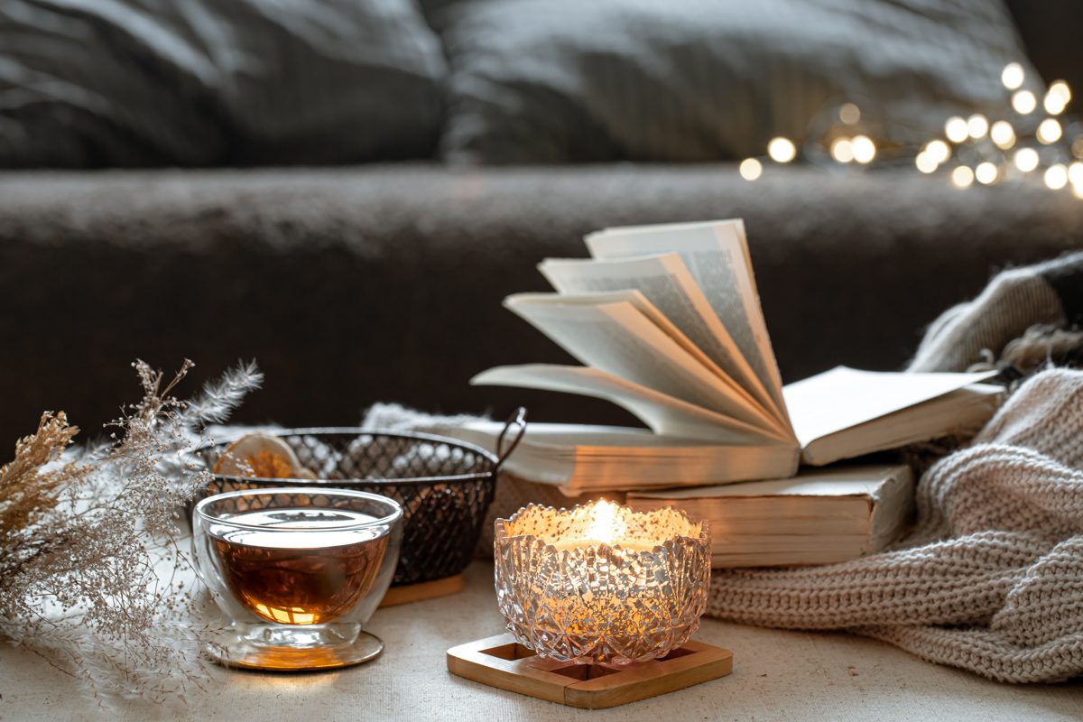 Glass cup of tea, an open book and a glowing candle on a winter evening
