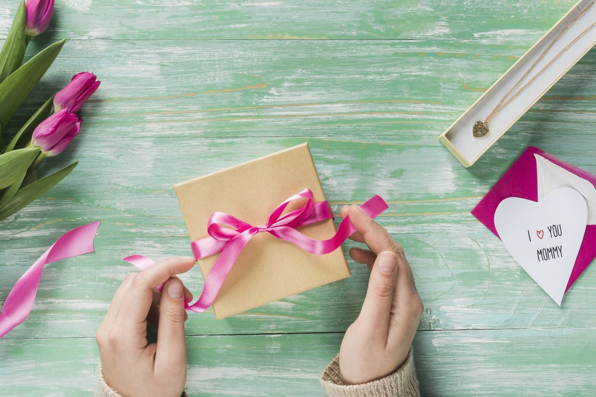Woman's hands tying a pink ribbon around a small kraft gift box
