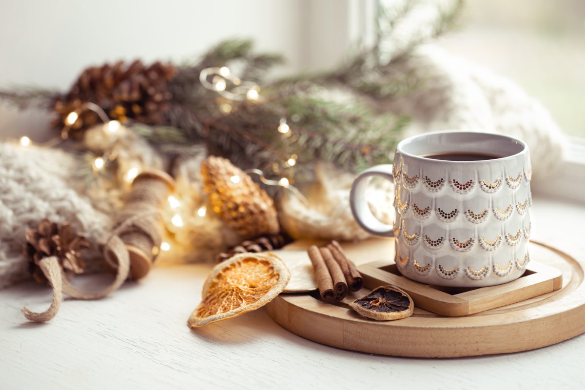Cozy mug with cinnamon and dried orange next to soft candlelight on a winter evening